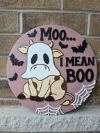 Halloween-themed sign with cow in ghost costume design and text 'Moo... I mean Boo' on a brick wall.