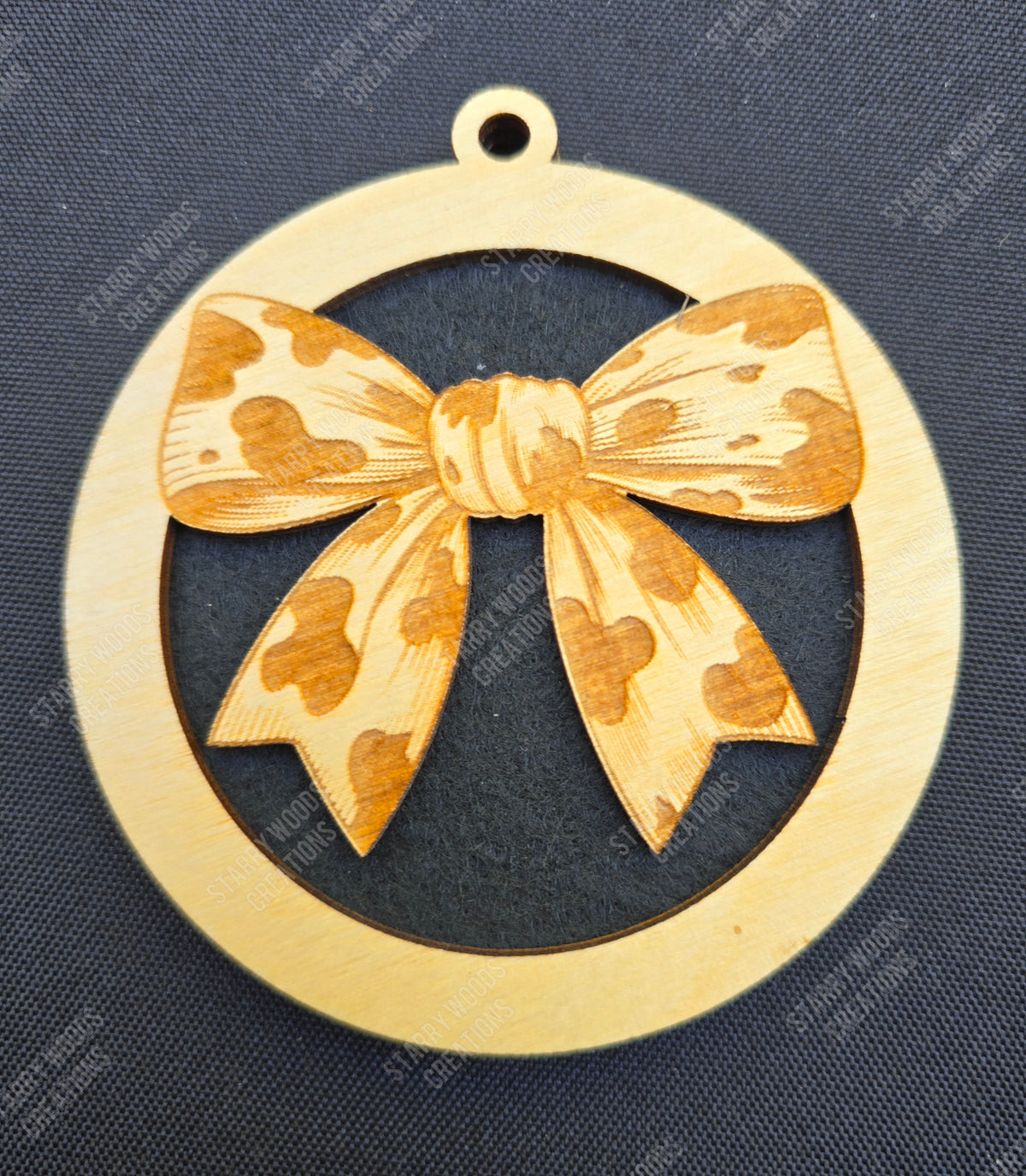 Wooden air freshener with cow print bow design on a dark blue fabric background