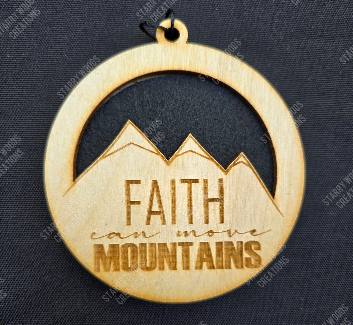 Wooden hanging air freshener with 'Faith can move mountains' text on a dark background