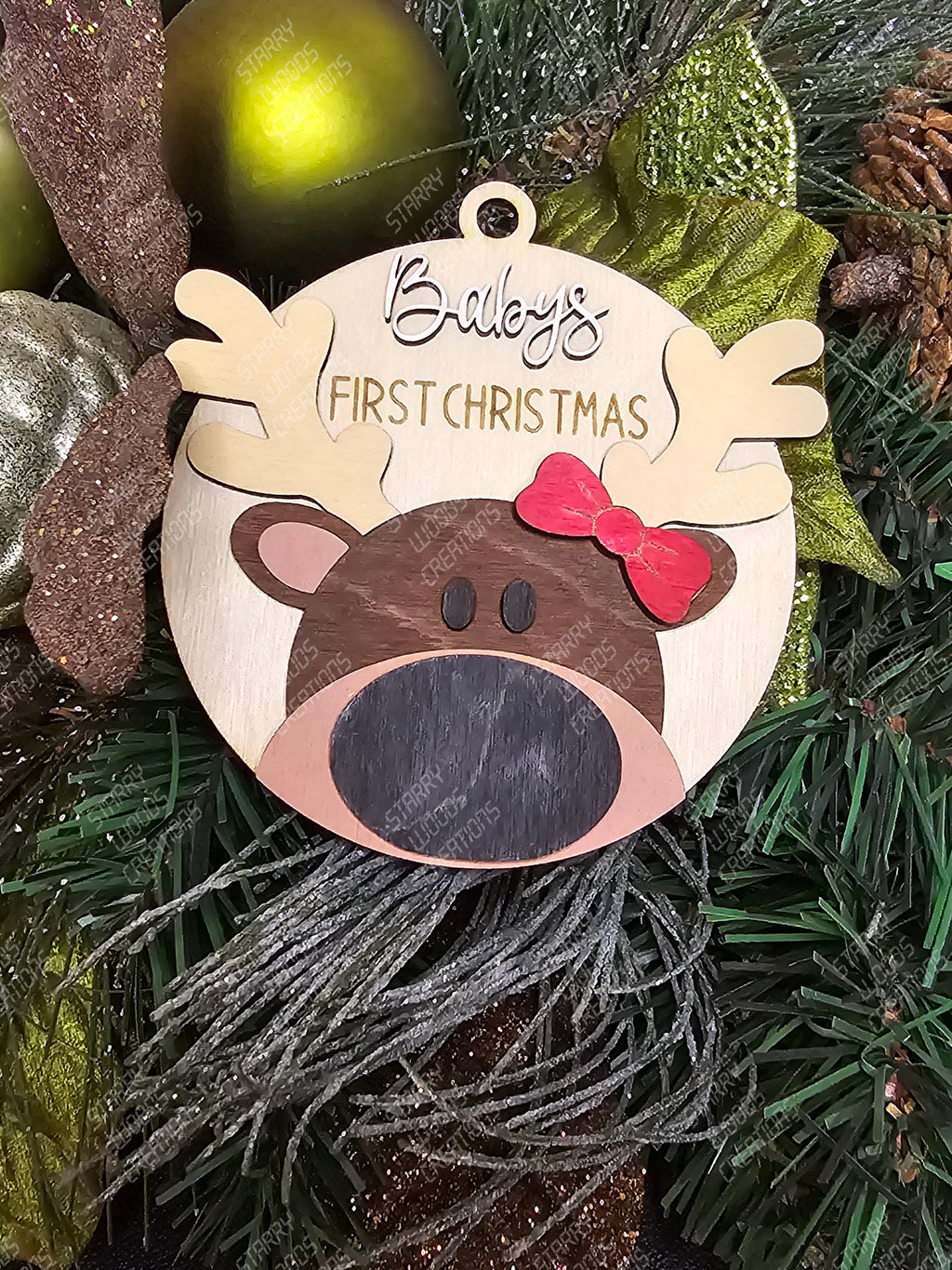 Decorative round ornament with reindeer design and 'baby's First Christmas' text on a Christmas tree. Reindeer has one red bow on antler. Handmade in Ontario and Customizable.