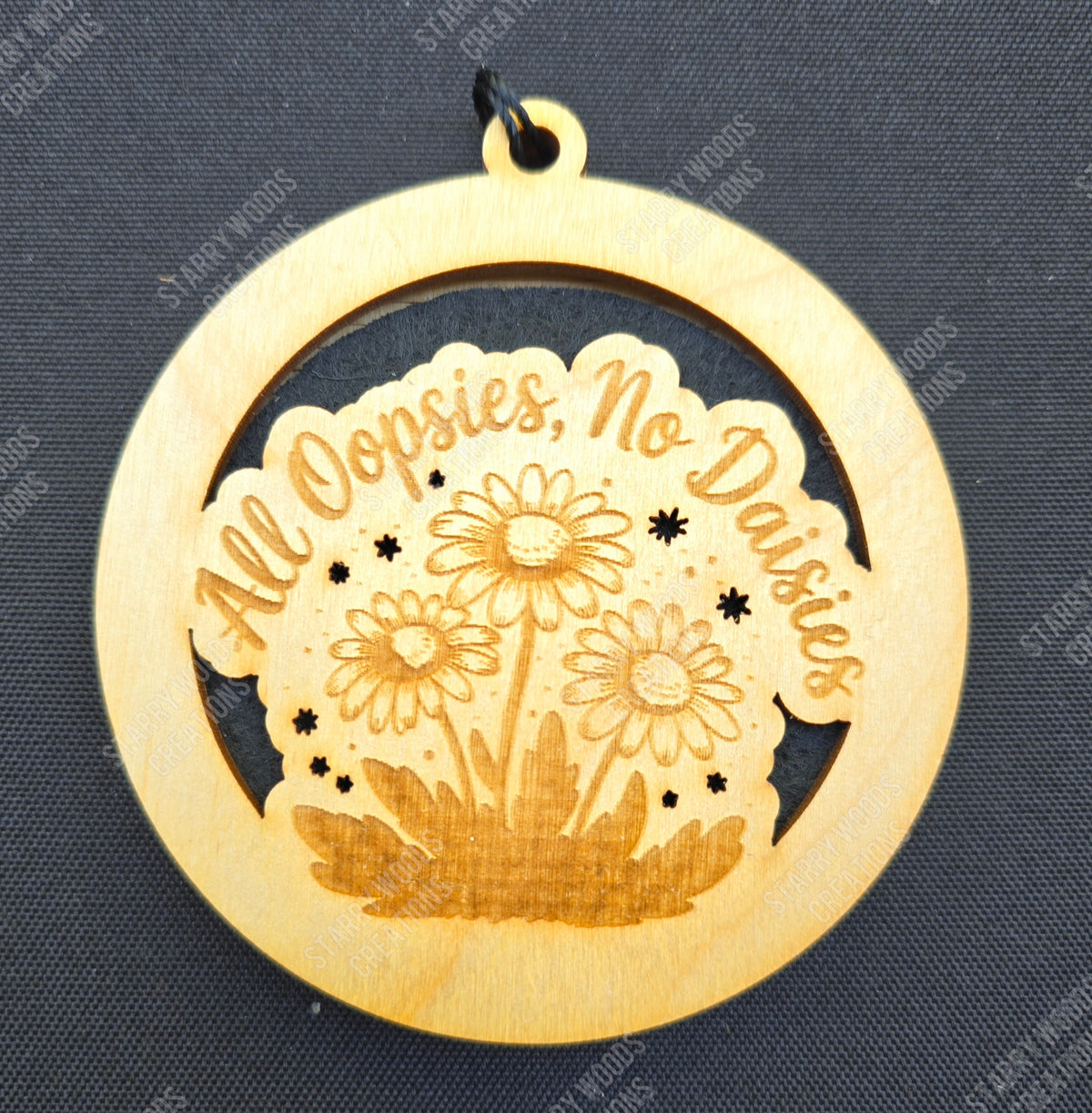 Wooden hanging air freshener with floral design and 'All Oopsies, No Daisies' text on a dark background