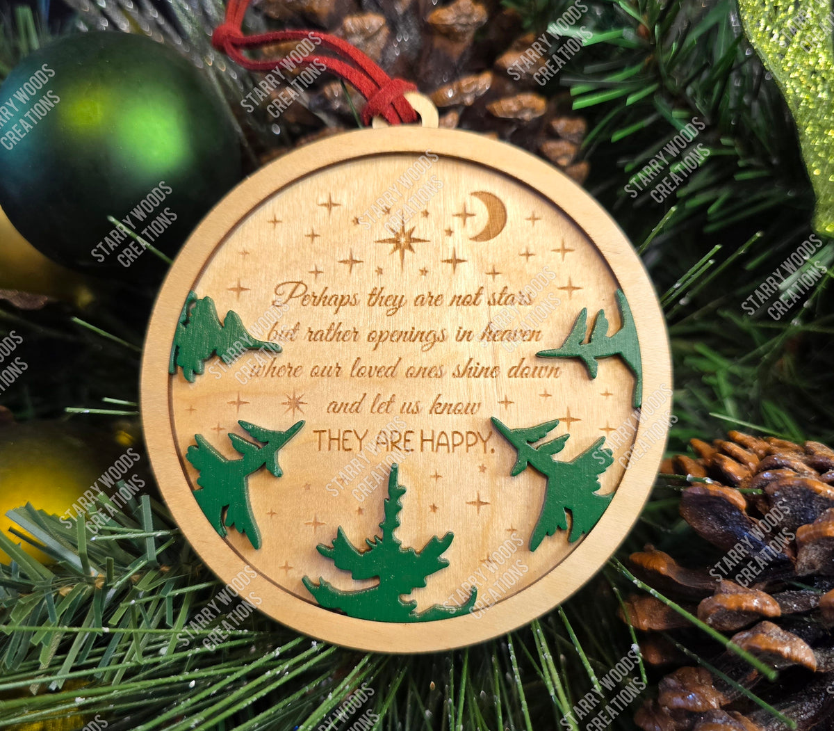 Round wooden memorial ornament with engraved text referencing stars as openings in heaven and green cut-out tree shapes on a Christmas tree background.