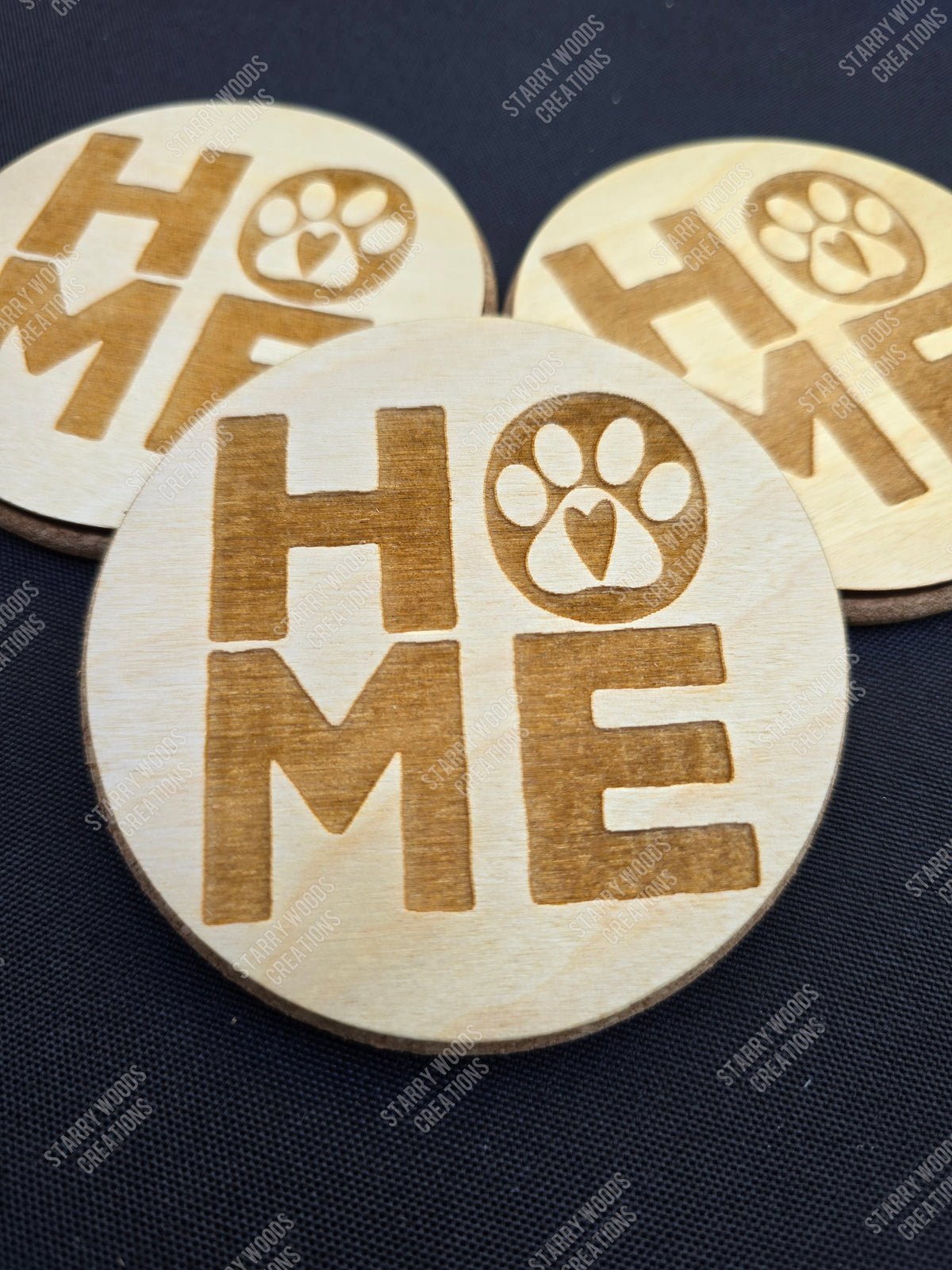 Round wooden coasters engraved with 'HOME' and paw print design on a dark fabric background
