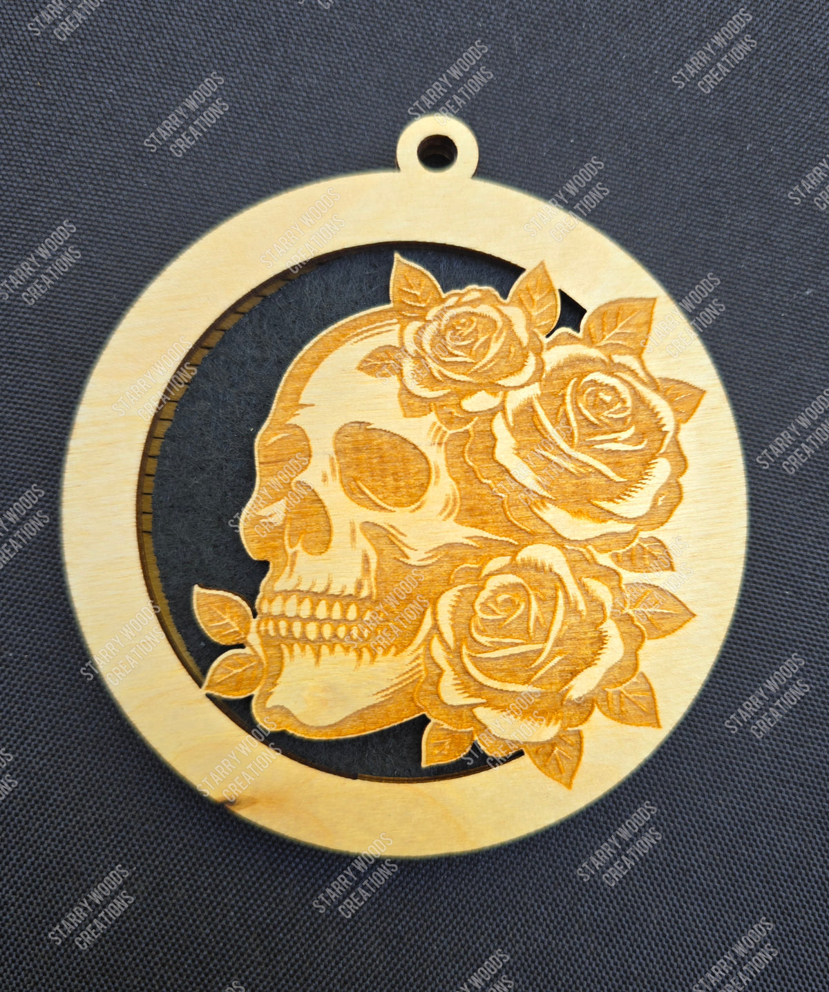 Woodem air freshener with a skull and rose design on a dark background