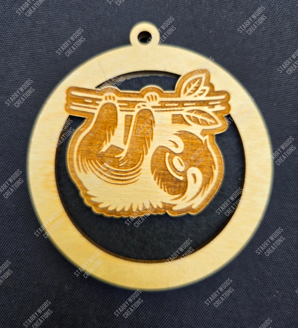 Wooden hangung air freshener with a design of a sloth on a branch against a dark background.